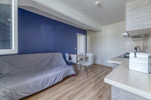 A modern room with a bed, a dining table, chairs, a kitchen area, and a large window.
