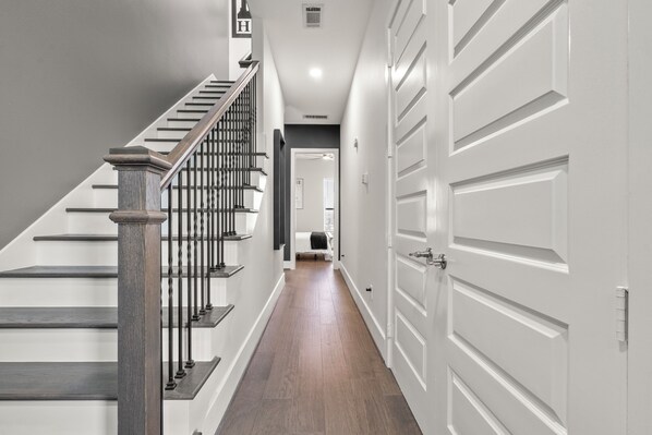 A modern hallway with a wooden staircase, white doors, and a neutral color scheme.