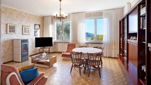 Uma sala de estar com televisão, sofá, mesa de jantar, cadeiras e estante de livros.