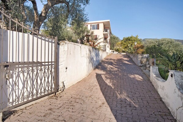 A paved pathway leading to a building with a white gate and a balcony.