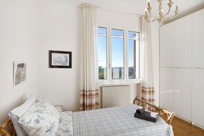 A bedroom with a bed, a window with curtains, a radiator, a wardrobe, and a chandelier. - Villa 'In Collina Vista Mare' with Sea View, Private Terrace and Garden (Sanremo)