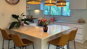 A modern kitchen with a central island, pendant lights, and a large window. - Noosa Heads House. Resort style pool, surrounded by tropical gardens. Location! (Noosa Heads)