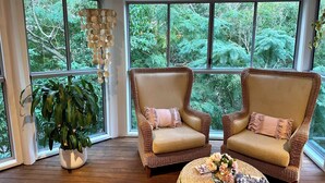 A room with two wicker armchairs, a large potted plant, and a round wicker table with a floral arrangement. - Noosa Heads House. Resort style pool, surrounded by tropical gardens. Location! (Noosa Heads)