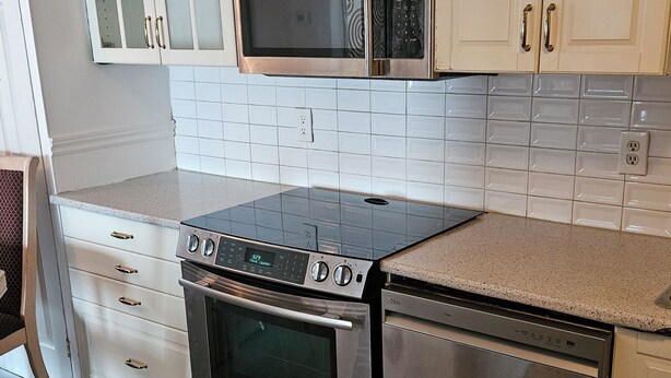 A modern kitchen with stainless steel appliances, white cabinetry, and a tiled backsplash. - Fully furnished house for rent for 6 to 8 people (Sainte-Thérèse)