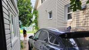 A black car parked on a brick driveway next to a house with white siding. - Fully furnished house for rent for 6 to 8 people (Sainte-Thérèse)