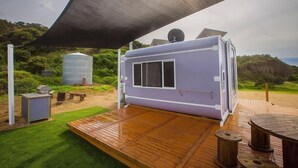A modern RV with a covered patio area, a satellite dish, and a small shed in a natural setting. - Hilltop Ocean View Pod (Marion Bay)
