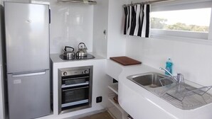 A compact kitchen with a built-in oven, a sink, and a kettle on the countertop. - Hilltop Ocean View Pod (Marion Bay)