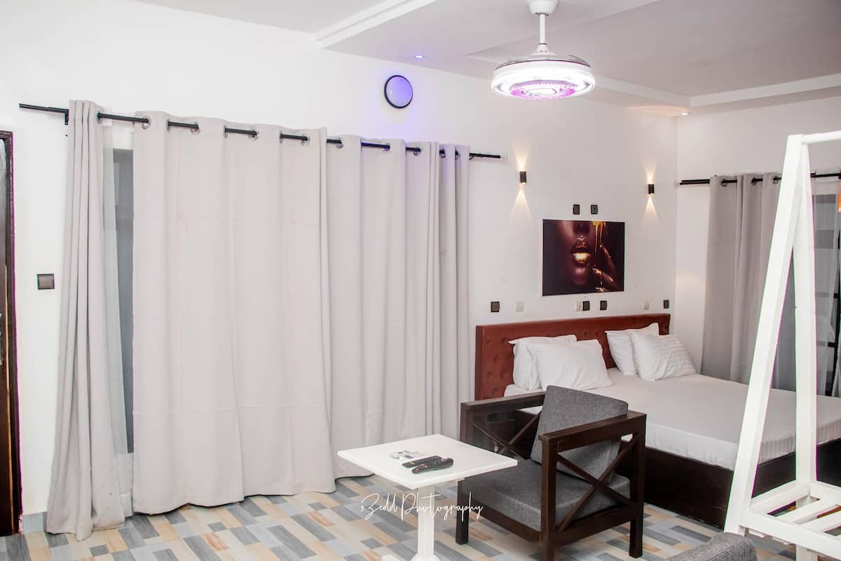 Une chambre d’hôtel avec un lit, une petite table avec une télécommande, une chaise et un miroir.