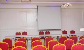 Una sala de conferencias con una pizarra, sillas rojas y una pantalla para proyector.