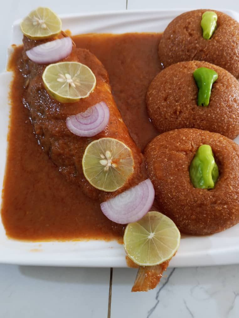 A plate with a fish fillet and four round items garnished with lime and green chili.