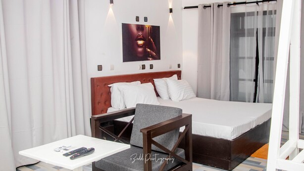 A hotel room with a bed, a chair, a small table, and a wall-mounted picture. - ASVA BEACH RESORT (Grand Popo)