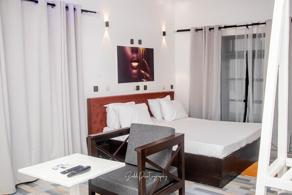 A hotel room with a bed, a chair, a small table, and a wall-mounted picture. - ASVA BEACH RESORT (Grand Popo)