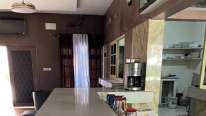 A modern kitchen with a marble countertop, a coffee machine, and a dining area with a long table. - ASVA BEACH RESORT (Grand Popo)