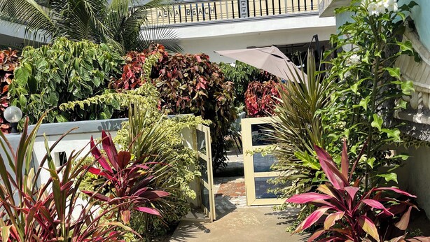 A courtyard with a variety of plants and a building with a balcony. - ASVA BEACH RESORT (Grand Popo)