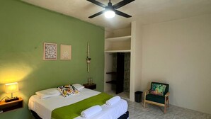 A hotel room with a bed, a ceiling fan, a nightstand, a chair, and a wardrobe. - Casa Chulibul located in downtown Merida, a fusion of tradition and comfort. (Centro)