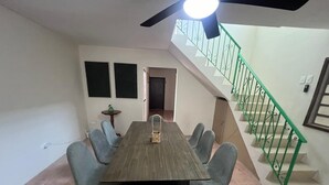 A dining area with a long table and six chairs, a ceiling fan, and a staircase with green railings. - Casa Chulibul located in downtown Merida, a fusion of tradition and comfort. (Centro)