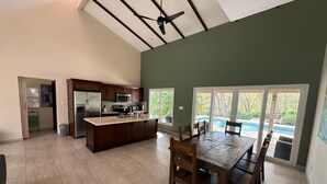 Une cuisine spacieuse avec un grand îlot central, un coin repas avec une table et des chaises en bois, et une vue sur une piscine grâce à des portes vitrées.