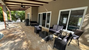 Une terrasse extérieure avec une table à plateau de verre, des chaises en osier et un barbecue.