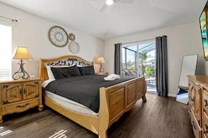 A bedroom with a wooden bed, bedside tables, a nightstand, a dresser, and a large window with curtains. - Magical Disney Retreat | Lake Berkley Resort & Pool (Kissimmee)
