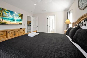 A hotel room with a large bed, a television mounted on the wall, a wooden cabinet, and a door leading to another room. - Magical Disney Retreat | Lake Berkley Resort & Pool (Kissimmee)