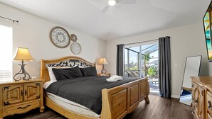 Ein Schlafzimmer mit einem hölzernen Bett, Nachttischen, einem Schminktisch und einer Kommode sowie einem großen Fenster mit Vorhängen.