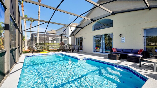 Ein Schwimmbad mit Glasveranda, Sitzgelegenheiten im Freien und Blick auf Palmen.