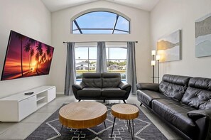 A modern living room with a large TV, two sofas, a coffee table, and a view of the outdoors. - Magical Disney Retreat | Lake Berkley Resort & Pool (Kissimmee)