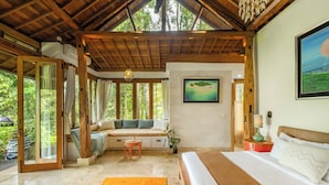 Un dormitorio amplio con una cama grande, techo de madera y vistas a vegetación exuberante.