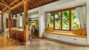 Una cocina amplia con vigas de madera, una zona de bar con taburetes y un rincón con ventanales y cojines.