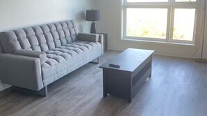 A modern living room with a grey sofa, a small table, and a floor lamp. - Executive Luxury Apartment. (Oakville)