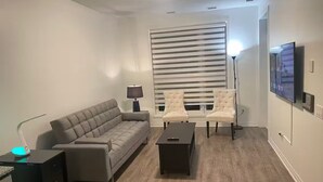 A modern living room with a grey sofa, two armchairs, a coffee table, and a TV mounted on the wall. - Executive Luxury Apartment. (Oakville)