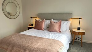 A neatly made bed with a grey headboard, two bedside tables with lamps, and a round mirror on the wall. - Midcentury 2br apartment in Toorak 
Close to MCG, Tennis, CBD 
 (Toorak)