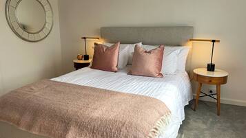 A neatly made bed with a grey headboard, two bedside tables with lamps, and a round mirror on the wall.