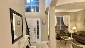 A spacious living area with a high ceiling, a staircase, a white door, a sofa set, and a coffee table.