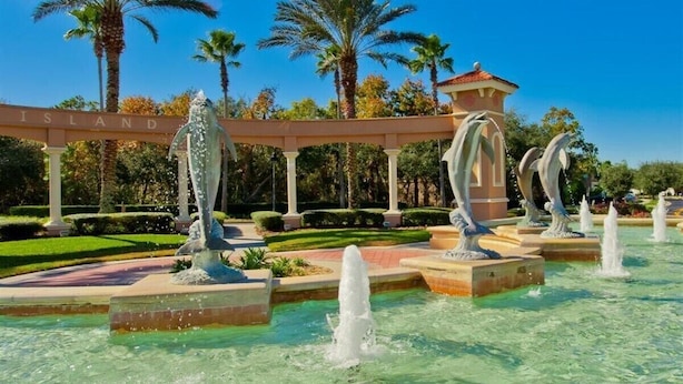 A fountain with multiple water jets and dolphin sculptures in a landscaped garden with palm trees and a gazebo.