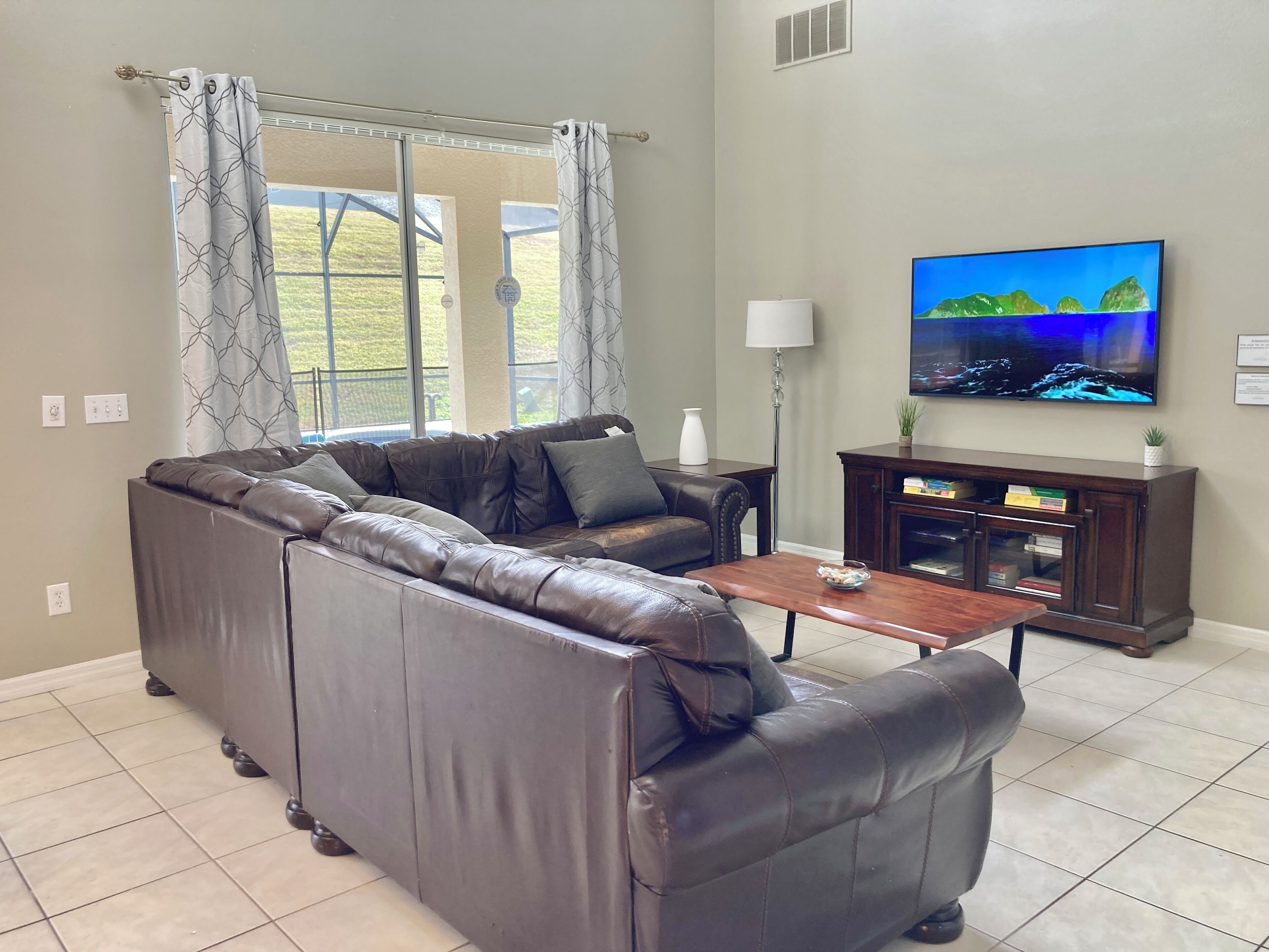 A living room with a leather sectional sofa, a wooden coffee table, a television, and a cabinet with books.