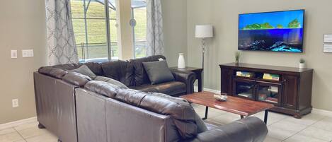 A living room with a leather sectional sofa, a wooden coffee table, a television, and a cabinet with books.