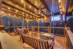 A wooden deck with outdoor seating, a fire pit, and string lights. - Sleeps 18, Private Heated Indoor Pool, Theater, Hot Tub, 20 Min to Dollywood (Sevierville)