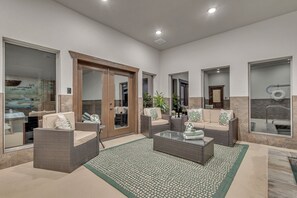 A spacious living area with wicker furniture, a glass coffee table, and a patterned rug.