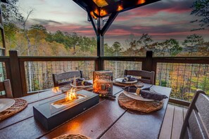 An outdoor dining area with a fire feature, a book titled "Campfire Cocktails," and a view of trees and sky. - Sleeps 18, Private Heated Indoor Pool, Theater, Hot Tub, 20 Min to Dollywood (Sevierville)