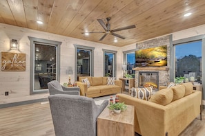 A modern living room with a fireplace, large windows, and a ceiling fan.