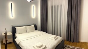 A modern hotel room with a neatly made bed, a bedside table with a lamp, and a large window with curtains. - Modern City Home w. A/C (București)