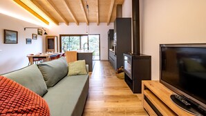 Ett modernt vardagsrum med ett träpanelat tak, en stor platt-TV, en soffa och en matplats med ett bord och stolar.