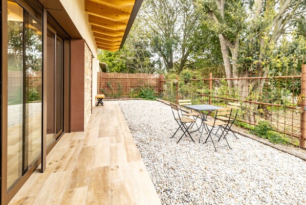 Un patio moderno al aire libre con una mesa y sillas, cerca de una valla de madera y una zona de grava.