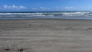 Uma praia com areal e ondas ao fundo.