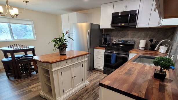 Een moderne keuken met houten vloeren, witte kasten, een inbouw eiland en een eethoek met een schaakbord.