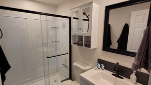 Een moderne badkamer met een douchecabine van glas, een wit toilet, een wastafel met spiegel en een inbouwkast.