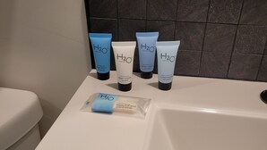 Een badkamer met een witte badkuip, een wand betegeld met zwart en vier H2O Therapy producten op de rand.