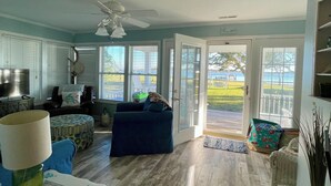 A spacious living room with a wooden floor, a blue sofa, and a dining area with a table and chairs. - Charming 2-bedroom cottage in Sneads Ferry with WiFi and AC (Sneads Ferry)