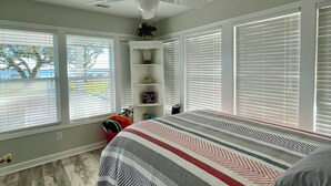 A bedroom with a bed, a ceiling fan, and large windows with blinds. - Charming 2-bedroom cottage in Sneads Ferry with WiFi and AC (Sneads Ferry)